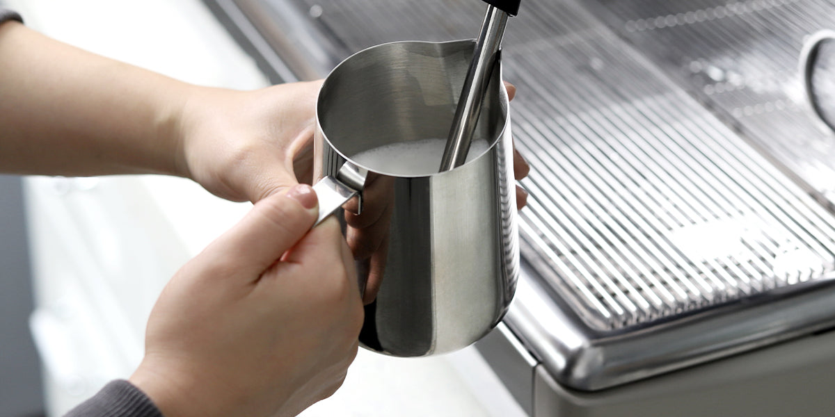 VEVOK CHEF stainless steel milk frothing pitcher in use with an espresso machine, frothing milk to a rich and creamy texture, ideal for lattes, cappuccinos, and other espresso-based drinks.